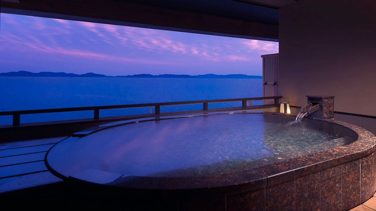 貸切露天風呂、石造りの丸型湯船と夕景